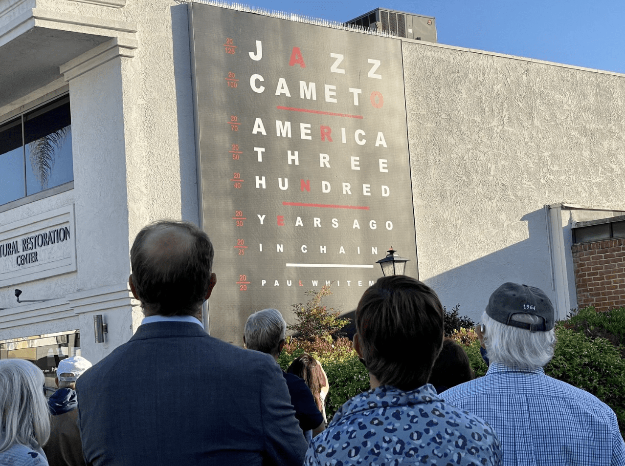 people looking up at a black mural with white and red text on the side of a building